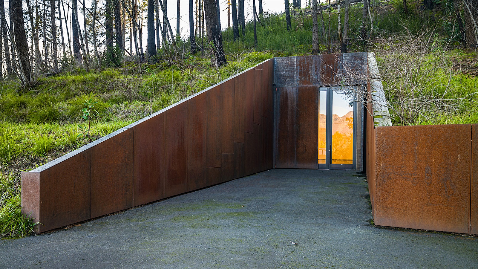  Exterior of the art cave on the former Stonescape estate, built into a wooded hillside and framed by dark wood